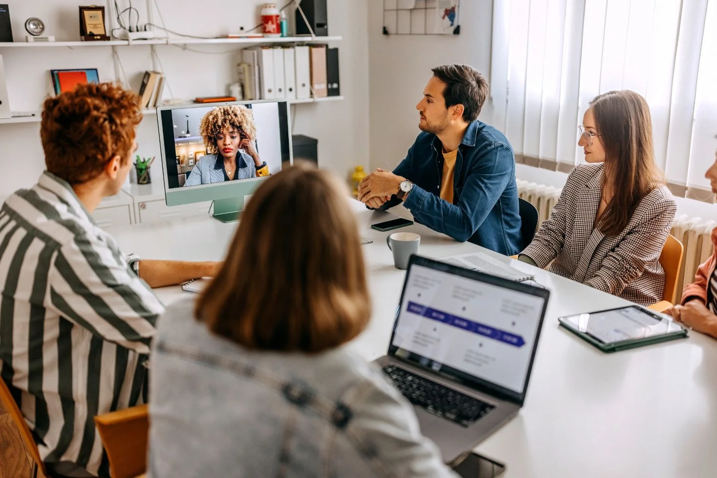several employees seated at conference table with their attention on an employee over Zoom