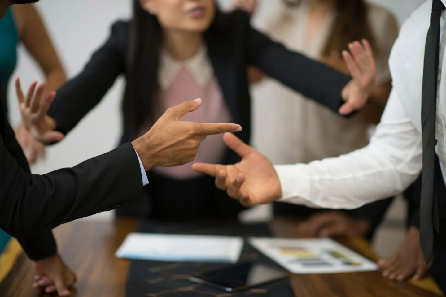 close up of the hands of people pointing at one another, in the background another person tries to calm them down