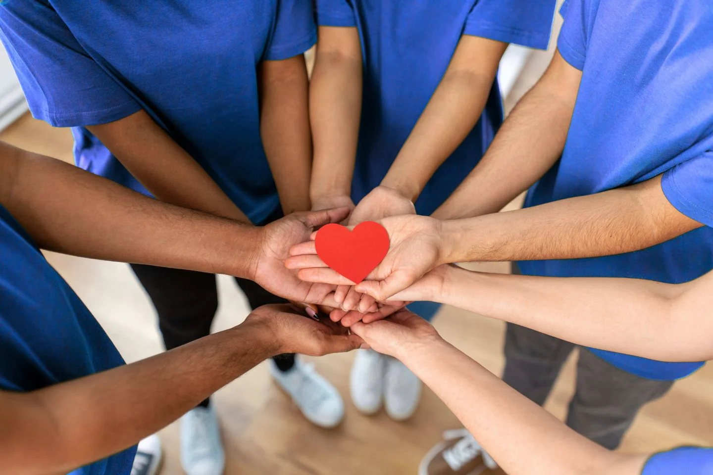 volunteers putting their hands into the center of a circle, palms upturned, holding a paper heart
