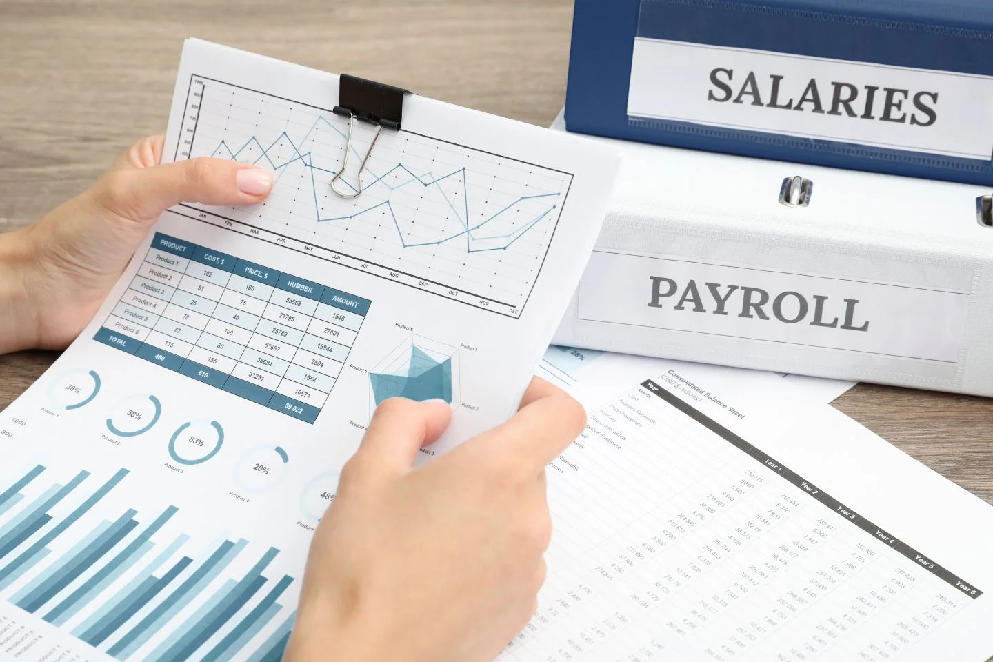 hands holding binder clipped financial documents in front of two binders - one labeled salaries, the other payroll
