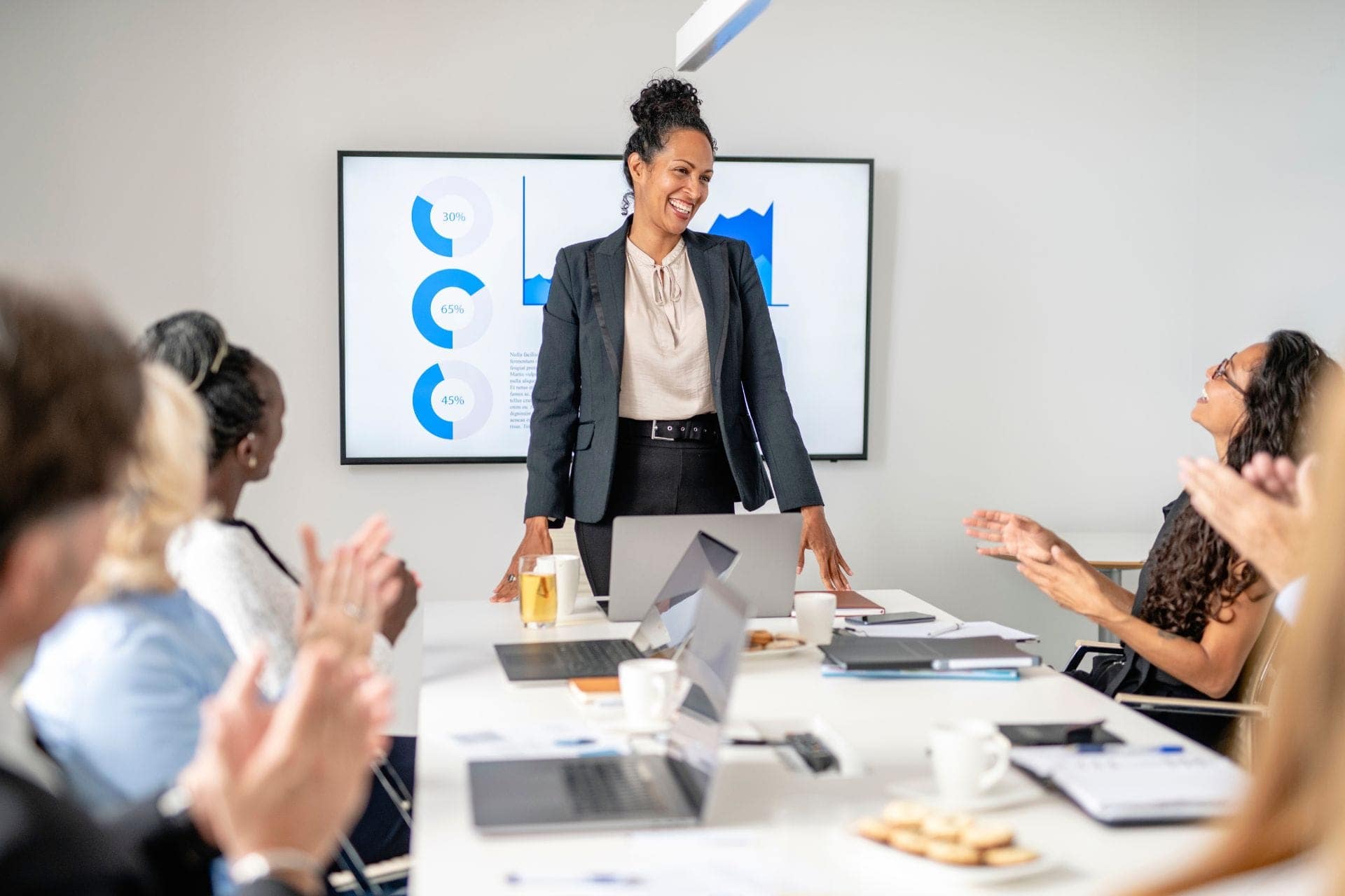 woman standing in front of a conference table at which colleagues are sitting